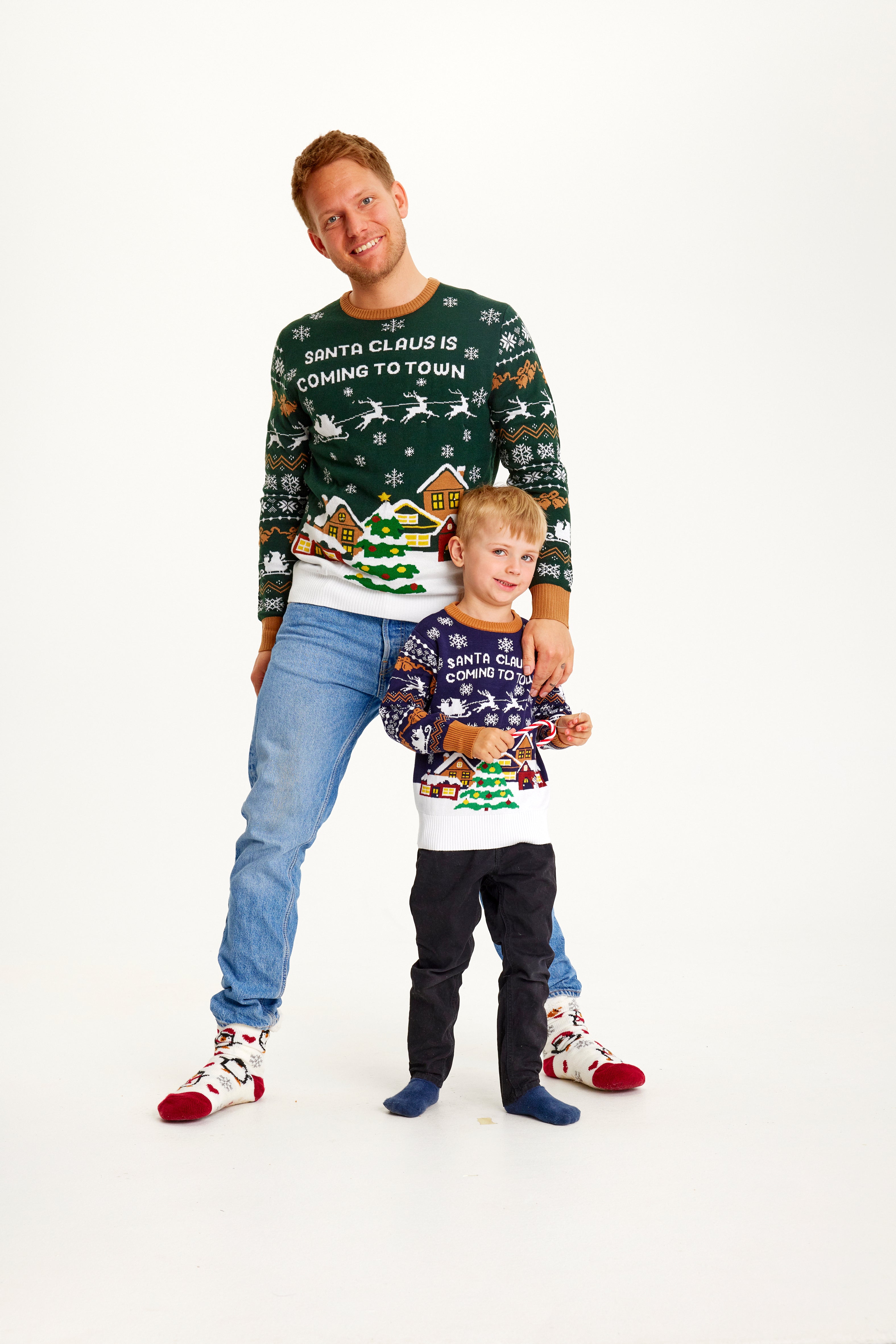 Een man en een kind poseren samen terwijl ze een kersttrui dragen met een besneeuwde stad.